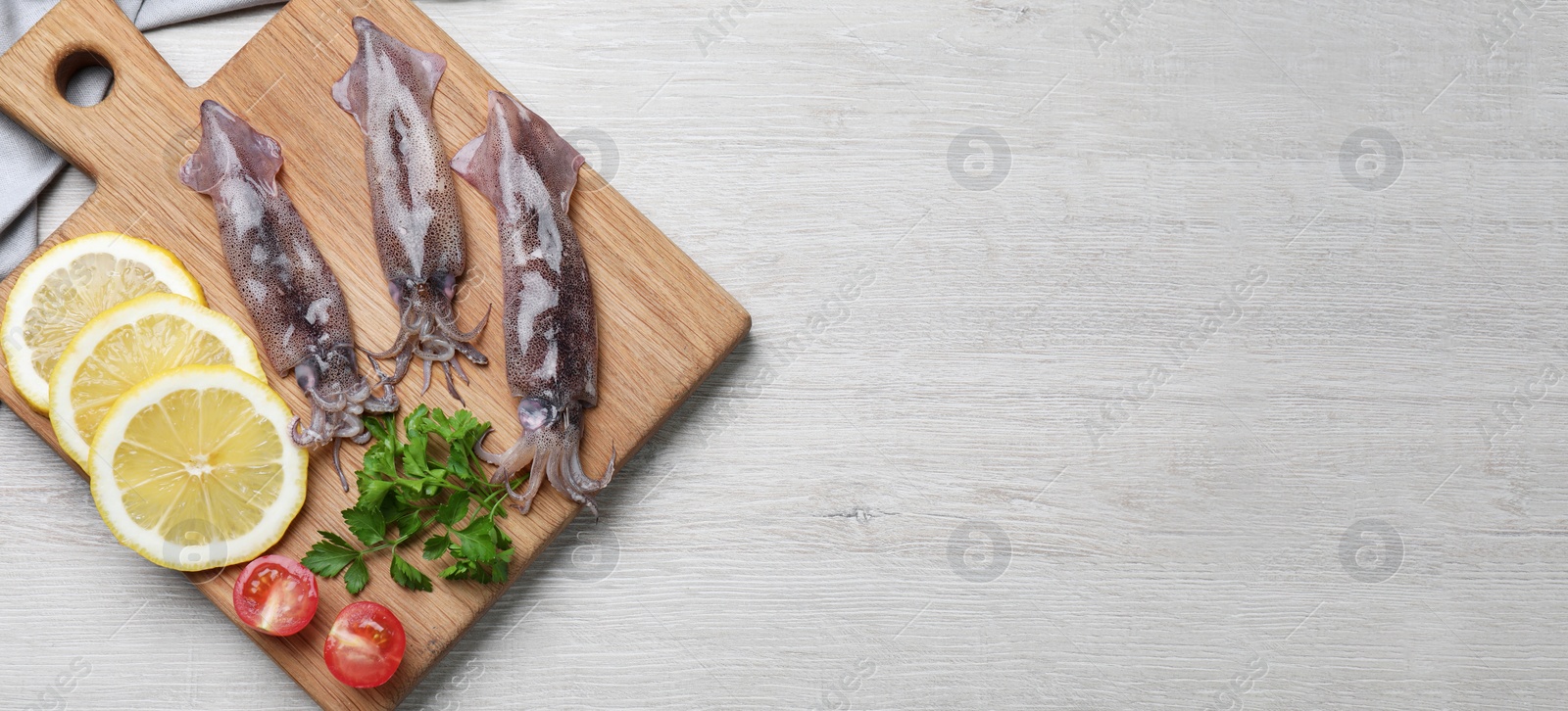 Image of Board with fresh squids, parsley, slices of lemon and tomato on white wooden table, flat lay. Banner design with space for text