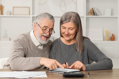 Photo of Elderly couple with papers discussing pension plan at wooden table indoors