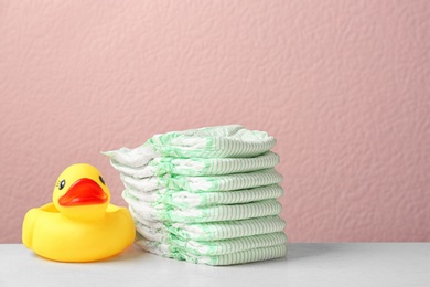 Photo of Stack of diapers and toy duck on table against color background, space for text. Baby accessories