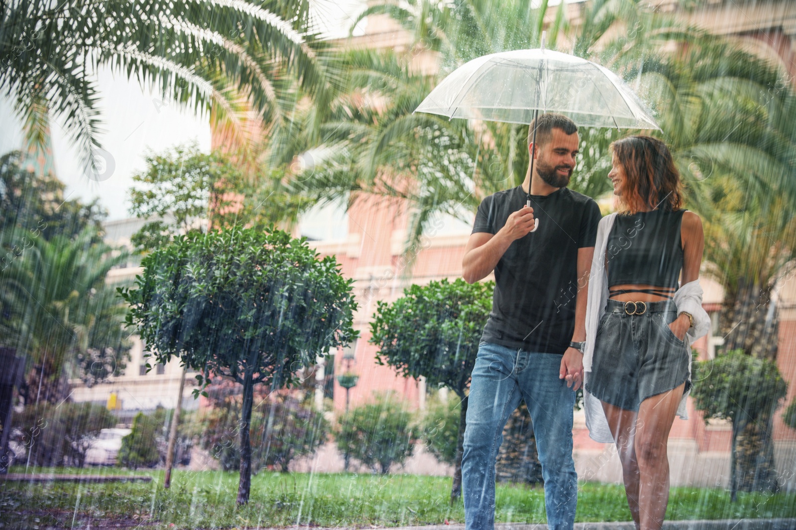 Image of Young couple with umbrella enjoying time together under rain on city street