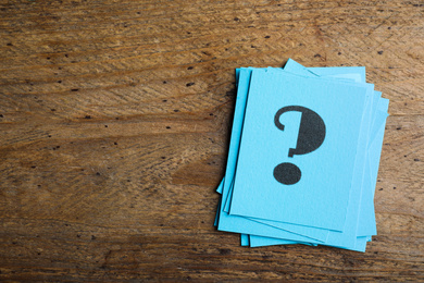 Photo of Blue paper cards with question mark on wooden background, top view. Space for text