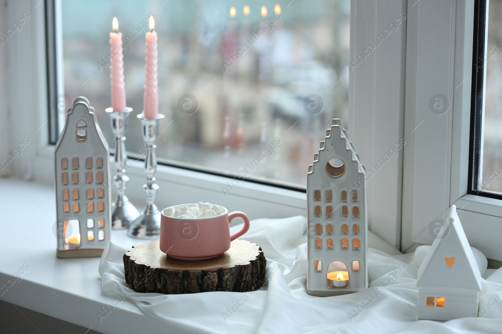 Photo of Beautiful house shaped candle holders and hot dink with marshmallow on windowsill indoors