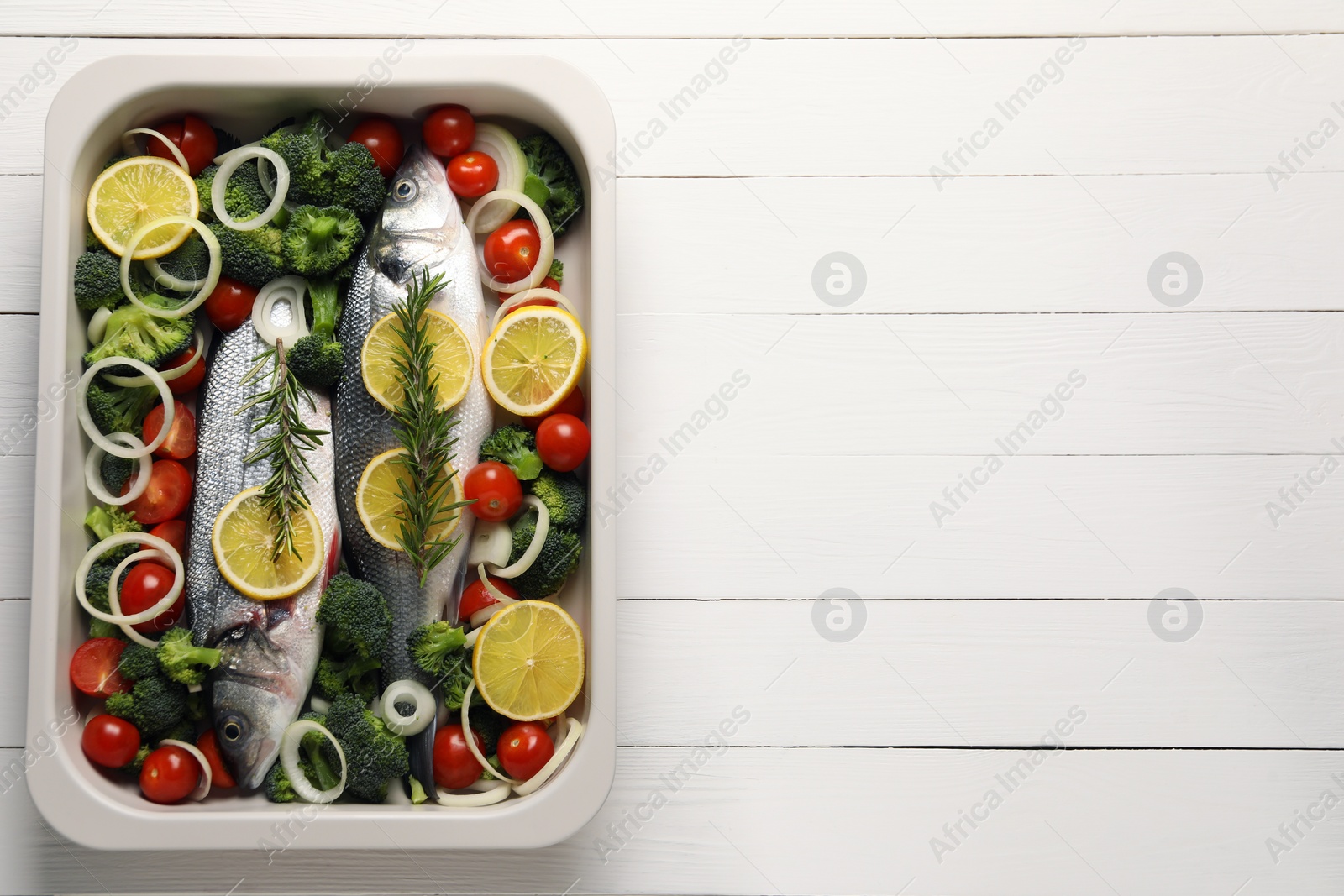 Photo of Raw fish with vegetables and lemon in baking dish on white wooden table, top view. Space for text