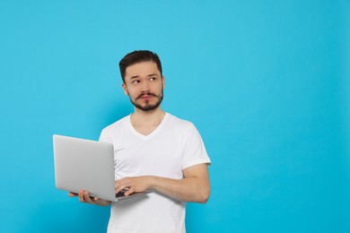 Photo of Pensive man using laptop on light blue background. Space for text