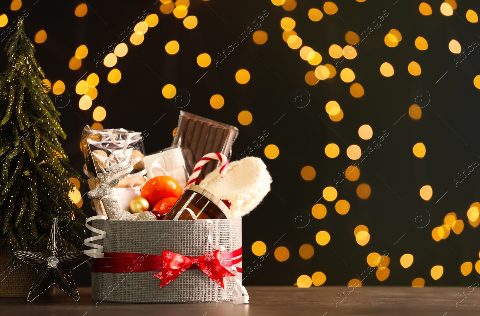 Photo of Basket with Christmas gift set on wooden table against blurred festive lights. Space for text