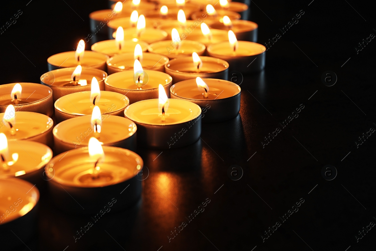 Photo of Wax candles burning on table in darkness, closeup