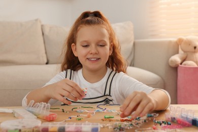 Photo of Cute girl making beaded jewelry at table in room