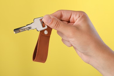 Photo of Woman holding key with leather keychain on yellow background, closeup