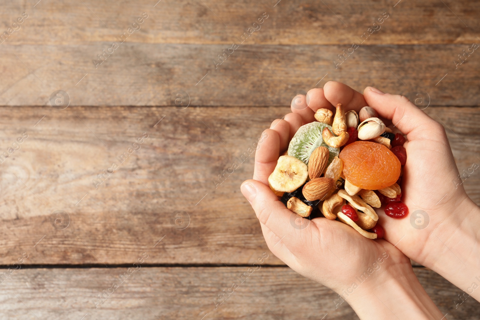 Photo of Woman holding different dried fruits and nuts on wooden background, top view. Space for text