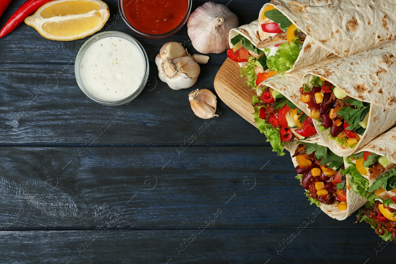 Photo of Board with delicious meat tortilla wraps on blue wooden table, flat lay. Space for text