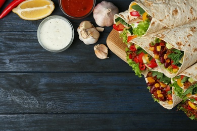 Photo of Board with delicious meat tortilla wraps on blue wooden table, flat lay. Space for text