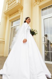 Young bride wearing wedding dress with beautiful bouquet outdoors