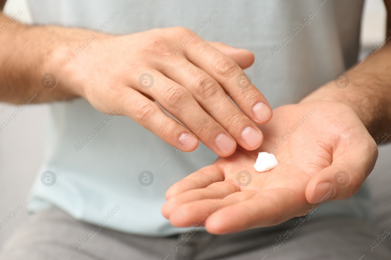 Photo of Man applying cream onto hand on blurred background, closeup