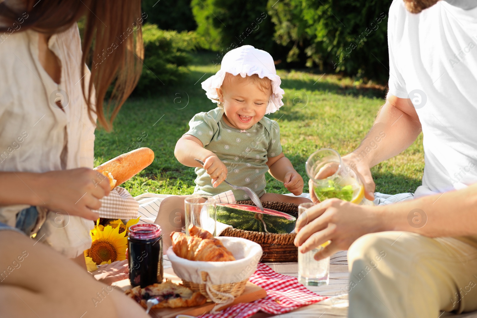 Photo of Cute child and her parents having picnic on sunny day in garden