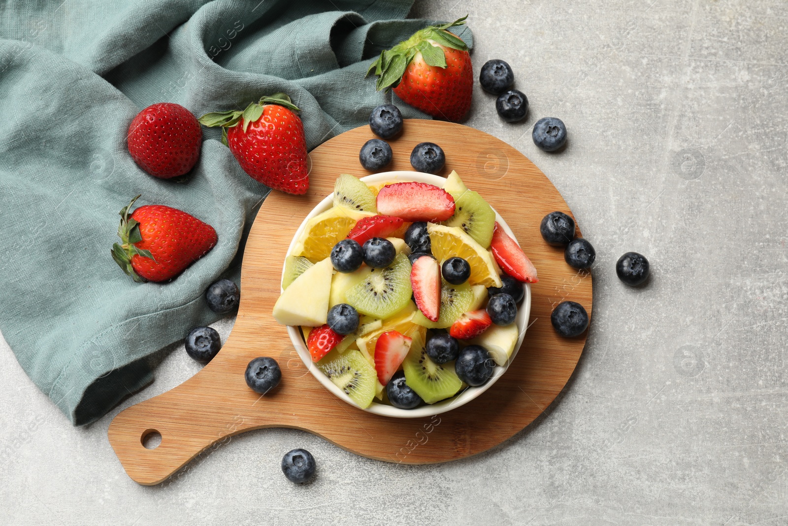 Photo of Tasty fruit salad in bowl and ingredients on gray textured table, flat lay