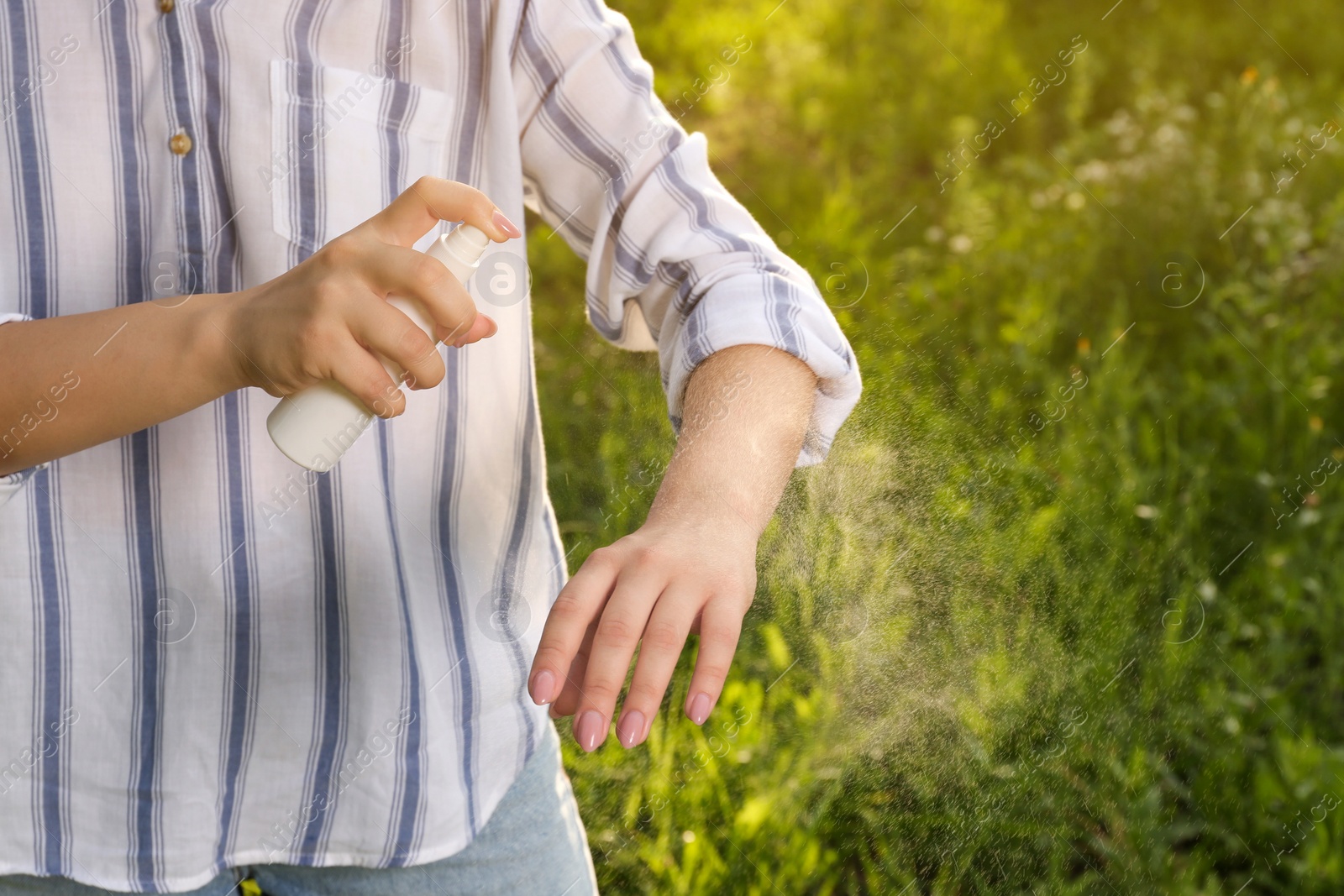 Photo of Woman applying insect repellent on arm in park, closeup. Tick bites prevention