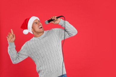 Photo of Happy man in Santa Claus hat singing with microphone on red background, space for text. Christmas music