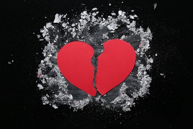 Halves of torn paper heart and ash on black background, top view