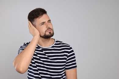 Young man suffering from ear pain on light grey background. Space for text