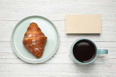 Photo of Croissant, coffee and blank card on white wooden table, flat lay. Tasty breakfast