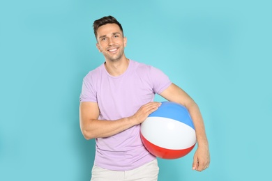 Happy young man with bright inflatable ball on blue background