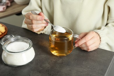 Woman adding sugar into aromatic tea at grey table, closeup