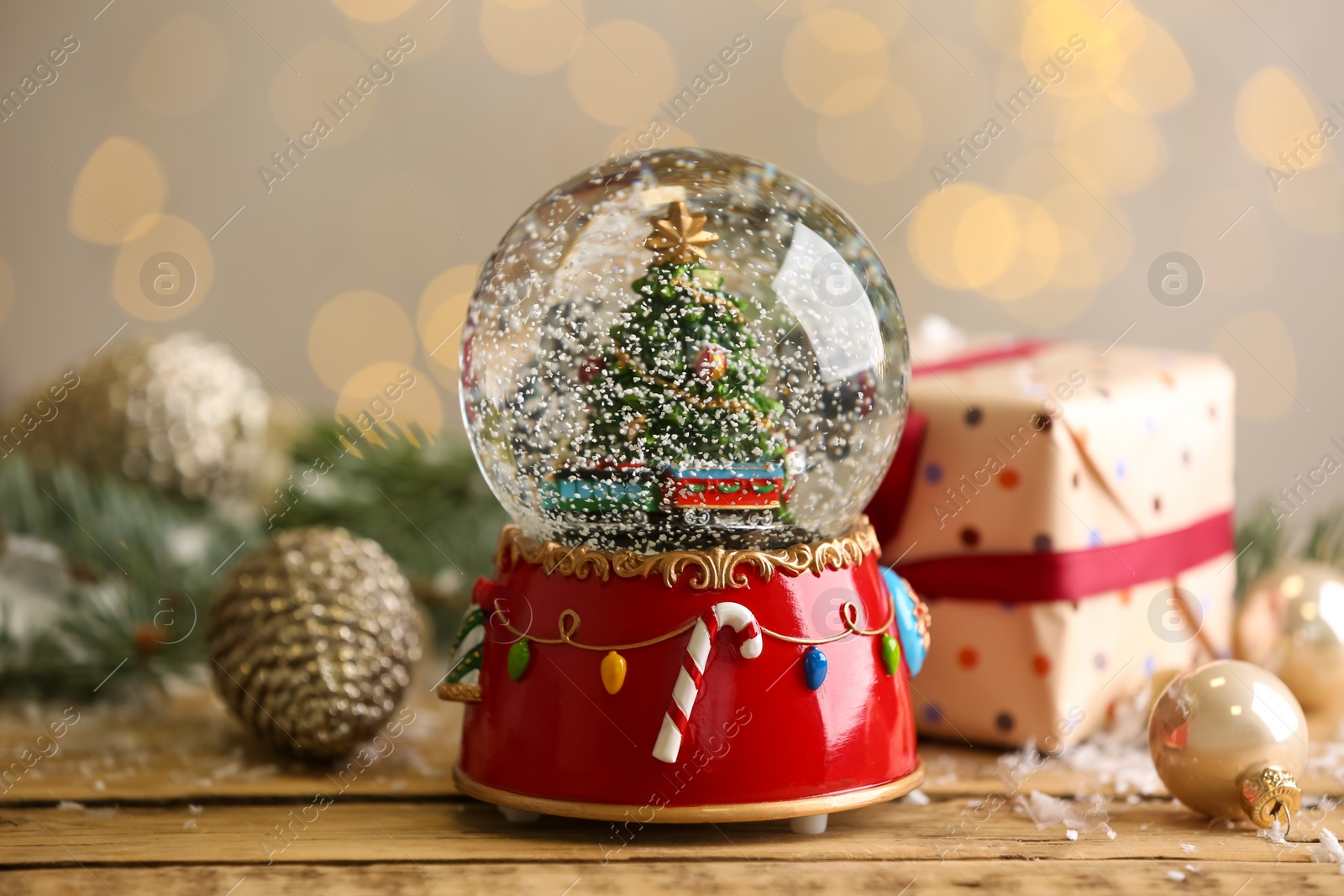 Photo of Beautiful snow globe with Christmas tree on wooden table against blurred festive lights