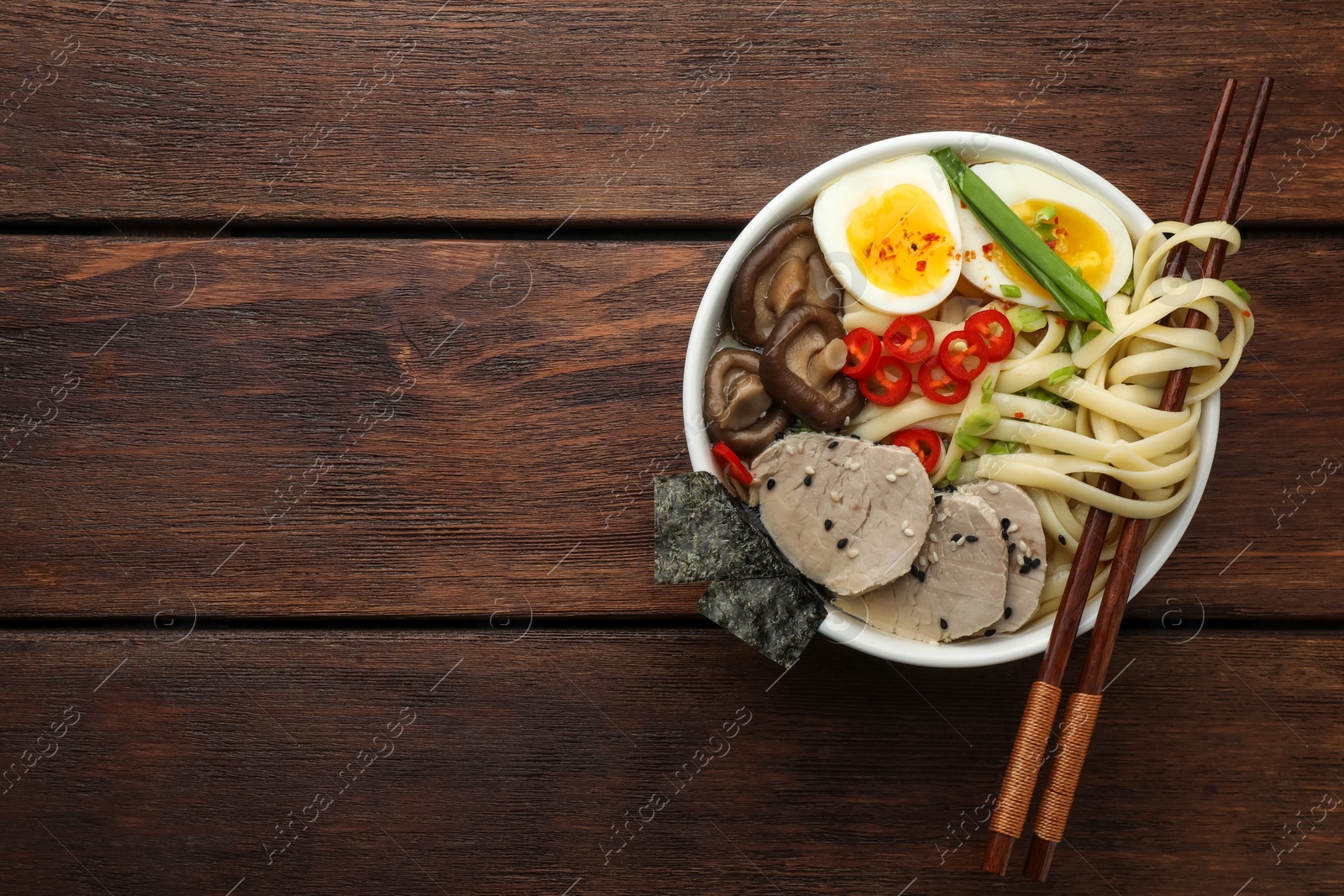 Photo of Delicious ramen with meat in bowl and chopsticks on wooden table, top view. Space for text. Noodle soup