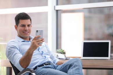 Photo of Businessman using smartphone in office chair at workplace