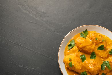 Photo of Tasty chicken curry with parsley on black textured table, top view. Space for text