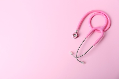 Pink stethoscope as awareness ribbon on color background, top view with space for text. Breast cancer concept