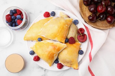 Photo of Delicious samosas with cherries and berries on white marble table, flat lay