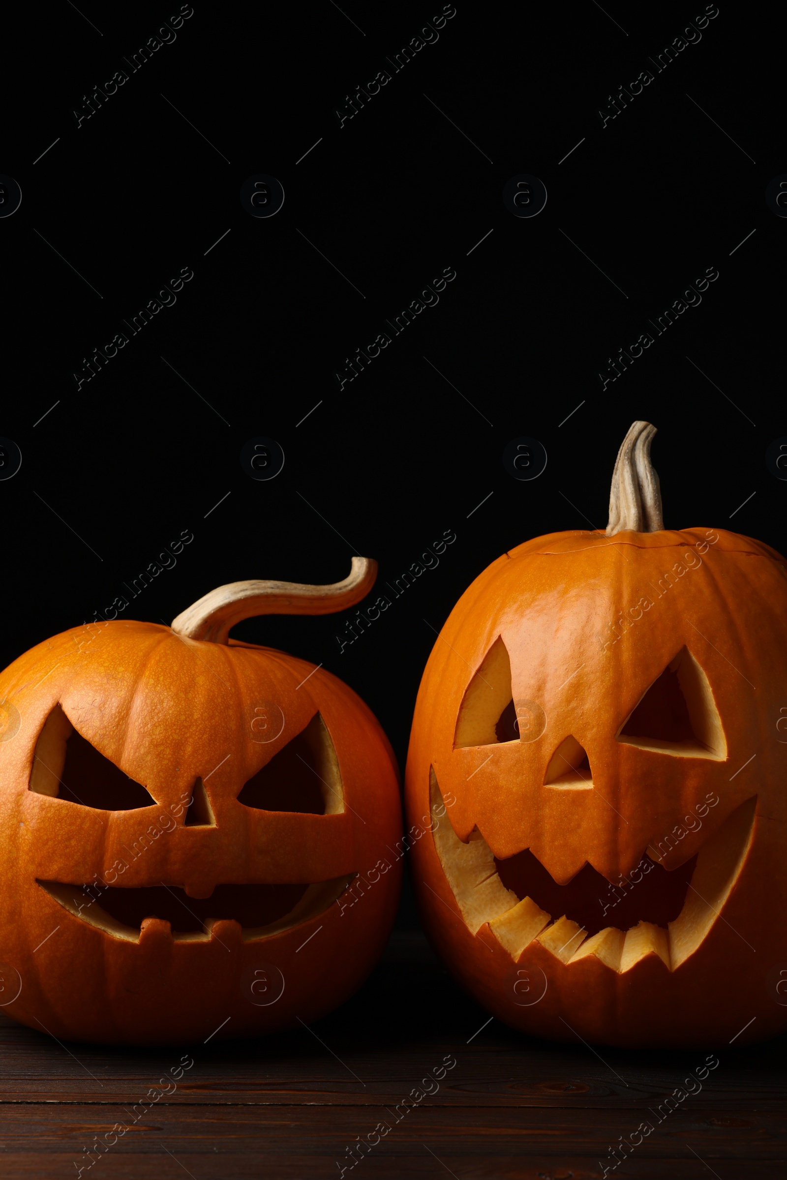 Photo of Scary jack o'lanterns made of pumpkins on wooden table in darkness, space for text. Halloween traditional decor