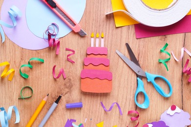 Photo of Paper birthday cake, confetti and stationery on wooden table, flat lay