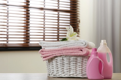 Photo of Clean towels with lily in basket and detergents on table indoors. Space for text