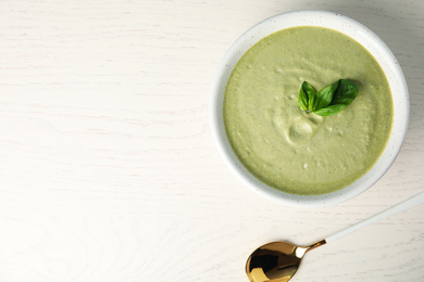 Delicious broccoli cream soup served on white wooden table, flat lay. Space for text