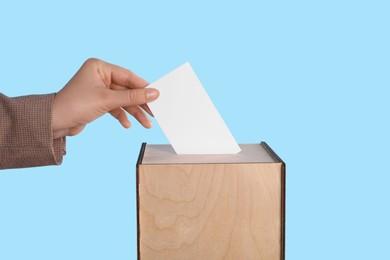 Photo of Woman putting her vote into ballot box on light blue background, closeup