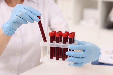 Doctor with samples of blood in test tubes at white table, closeup