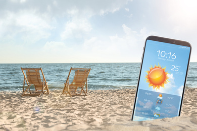 Wooden deck chairs on sandy beach and smartphone with open weather forecast app 