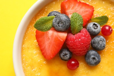 Photo of Delicious creme brulee with fresh berries on yellow background, closeup