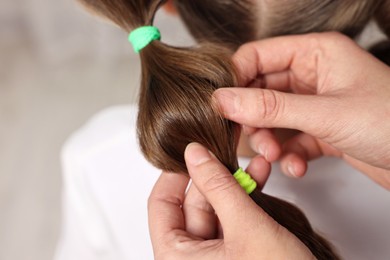 Professional stylist braiding girl's hair indoors, closeup