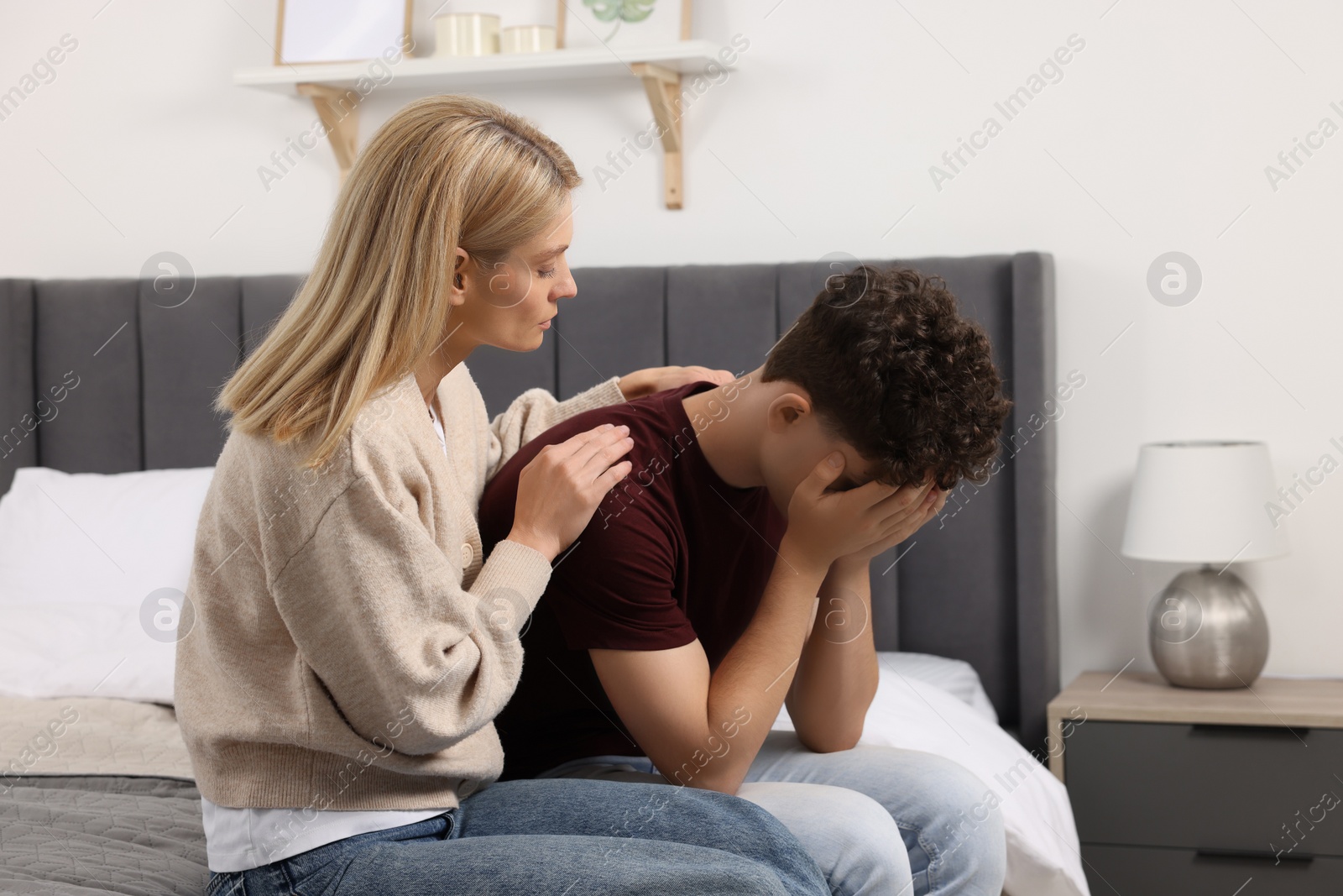 Photo of Mother consoling her upset son in bedroom. Teenager problems