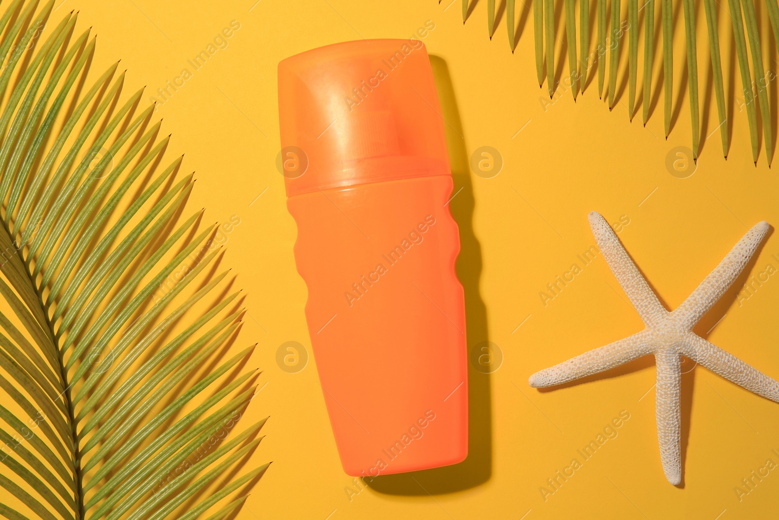 Photo of Sunscreen, starfish and tropical leaves on yellow background, flat lay. Sun protection care