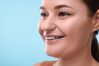 Smiling woman with dental braces on light blue background, closeup. Space for text