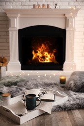 Photo of Cup of coffee, glasses and book on tray near fireplace indoors. Cozy atmosphere