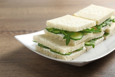 Photo of Plate with cucumber sandwiches on wooden table, closeup. Space for text