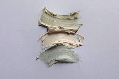 Photo of Samples of face mask on lilac background, flat lay