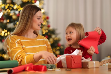 Photo of Christmas presents wrapping. Mother and her little daughter decorating gift box with ribbon at home