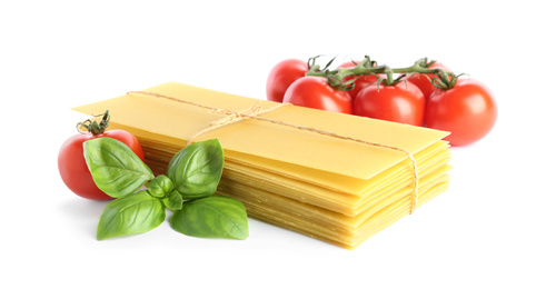 Photo of Uncooked lasagna sheets, tomatoes and basil on white background
