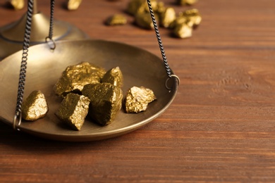 Photo of Scale pan with gold lumps on wooden table, closeup. Space for text